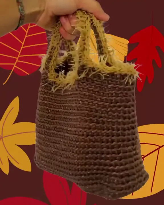 La borsa cioccolato all'uncinetto con i manici senape, tenuta a mano su un fondo di foglie d'autunno