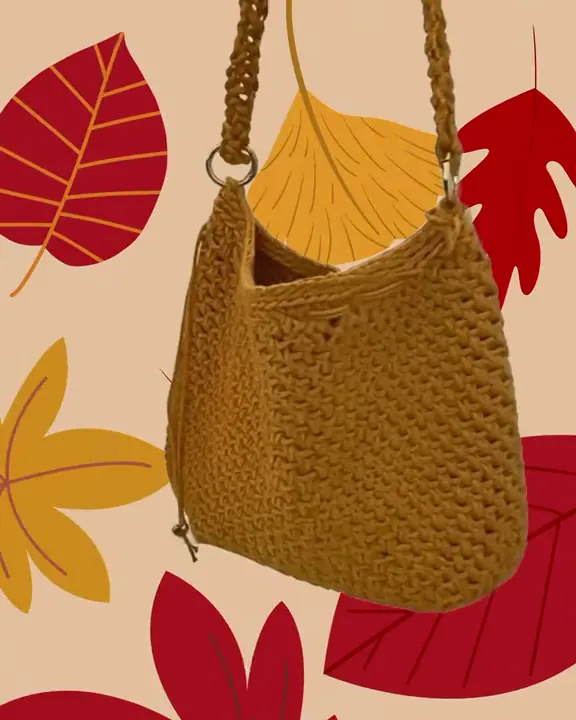 La borsa senape a tracolla all'uncinetto, con la tracolla intrecciata, su un fondo di foglie d'autunno